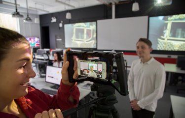 Student filming in the newsroom on a smartphone.