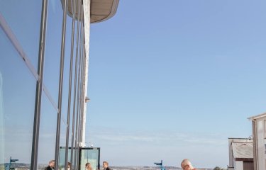 People sat at benches outside with a glass building to the right