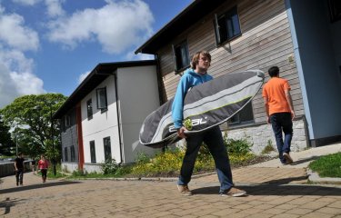 Student carrying surfboard outside student accommodation.