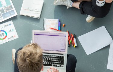 Two Falmouth University students sitting on the floor with a laptop and pieces of paper