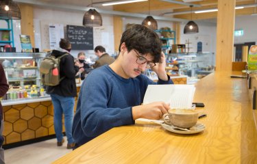 A student reading at a table in the cafe on Penryn Campus
