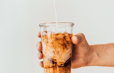 Photo of hand holding out a glass of iced coffee. Photo by Tavis Beck.