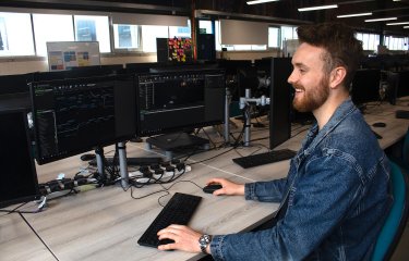 A Falmouth University Games student smiling at a computer screen with a keyboard and mouse