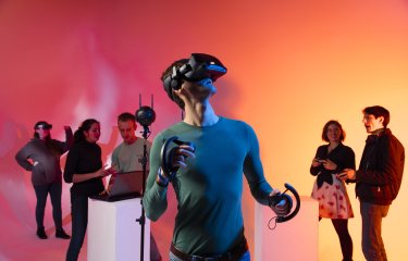 Games Academy students wearing a VR headset in front of an orange background