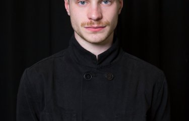 Student portrait - a white man with short hair poses in black clothing