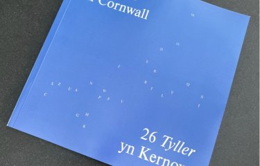Photo of 26 Cornwall book - light blue cover with A-Z of letters scattered in the shape of Cornwall  in white. Title reads: 26 places Cornwall / 26 Tyller yn Kernow