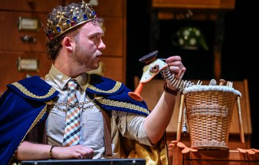 A person on stage performing wearing a crown and using a puppet duck