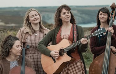 4 musicians holding instruments set against the rugged Cornish cliffs
