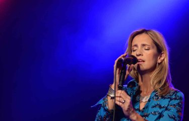 A person stood on stage under lighting singing into a handheld microphone