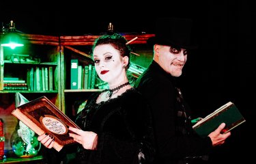 Two performers dressed in gothic costumes holding books and looking at the camera