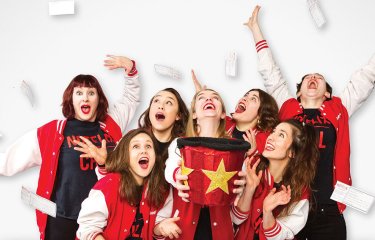 A group of performers posing in red outfits on a white background on top of the Notflix logo
