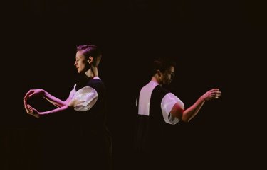 Two dancers wearing black and white costumes dancing against a black background