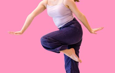 An image of a young female dancer jumping in the air against a bright pink backdrop