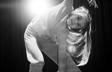 A black and white image of a young dance posing for the camera with a bright light in the background