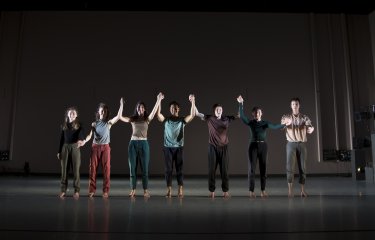 A line of dance students holding hands on a stage