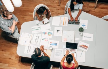 Birds eye view of group of people sat around a table with business strategy papers