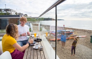 Falmouth University students sat on the terrace at Gylly Beach Cafe with the sea in the background