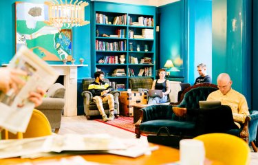 A group of students seated on sofas in a blue room with book cases and art on walls