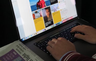 Hands typing on a laptop with a newspaper on a table