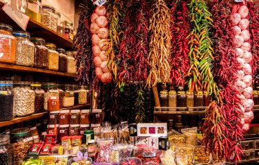 Spices and garlic hang from a market stall, with jars of dried goods surrounding the stall