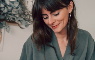 A woman with dark hair looking down and wearing an olive green top