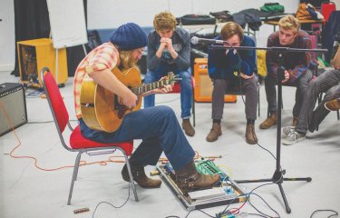 A man plays his guitar in front of three young men