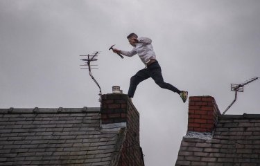 Photo of a man holding a hammer jumping from one rooftop to another during a protest in Manchester. 