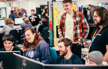 A group of games students smiling and laughing around a computer