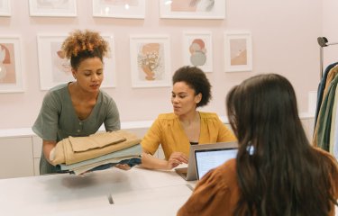 Three Sustainable Fashion students looking at fabric