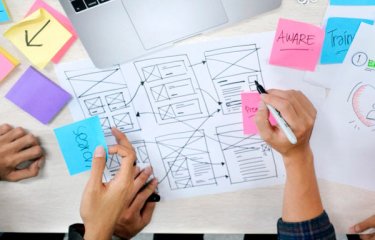 hands sketching a sitemap with a laptop and coloured post-it notes on a table