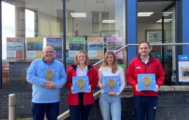 Four people standing outside Stuart Line Cruises shop front, holding a book with a dinosaur on the cover