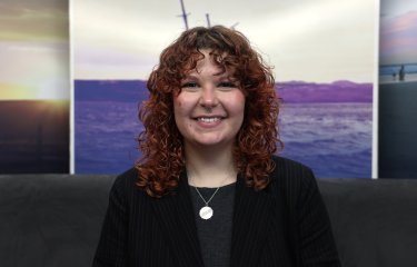 A woman smiling at the camera with a landscape picture in the background