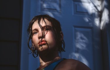 Photograph of a girl with dark wet hair with the sun on her face