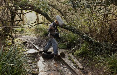 A person walking in a woodland with a large microphone