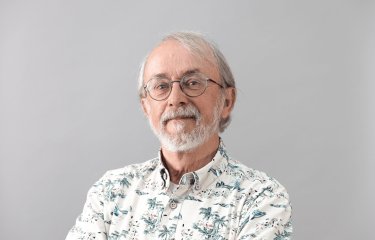 Headshot of Peter Lord against a grey background with a flowery shirt and glasses and a beard