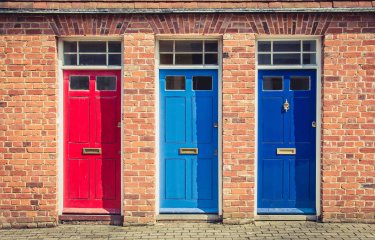 A row of 3 colourful front doors on a brick building
