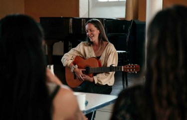 A musician sat in front od a piano playing an acoustic guitar