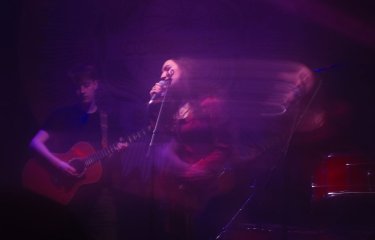 A photo of people performing which is slightly blurred with pink and purple lighting