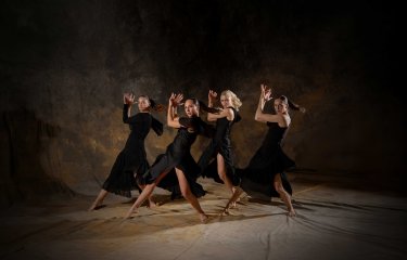 4 female dancers posing on a staged background wearing all black