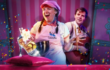 A performers in an ice cream booth with an ice cream sundae in a glass slipper in the front of the image