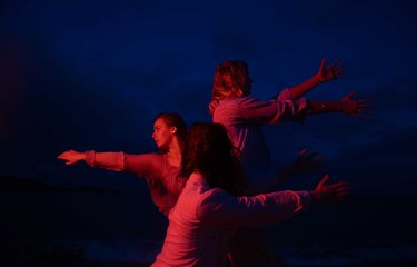 A dark and moody image of 3 dancers performing outside with a red light on them