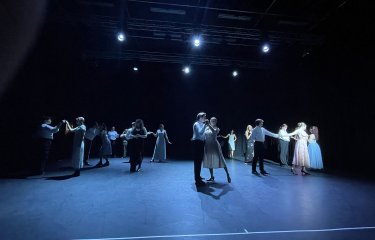 A large group of dance performers in a duet formation on stage under blue lighting