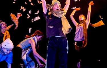 Children dancing and performing on stage throwing feathers into the air