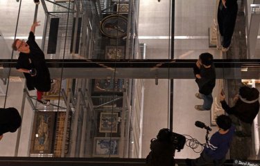 A Birdseye view looking down on performers on a glass floor above a museum gallery