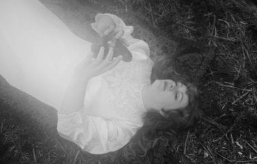 A black and white image of a person laying on the floor in a white dress holding an object