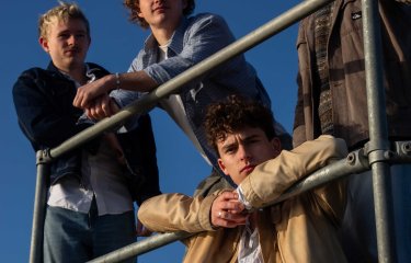A group of 4 leaning against a metal bar with blue sky in the background
