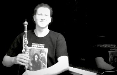 A black and white image of a person sat down with a clarinet on their knee