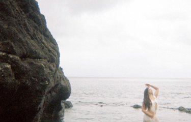 A person posing in the sea with water up to their waist with rocks on the left