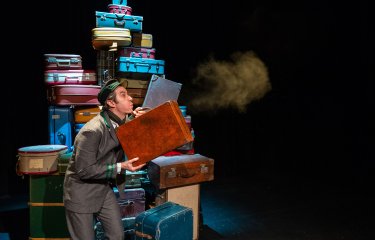 A person stood in front of a big pile of suitcase blowing dust off on one into the distance