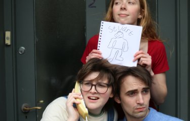 An image of 3 people. One on the phone, one holding a flower and one holding a piece of paper